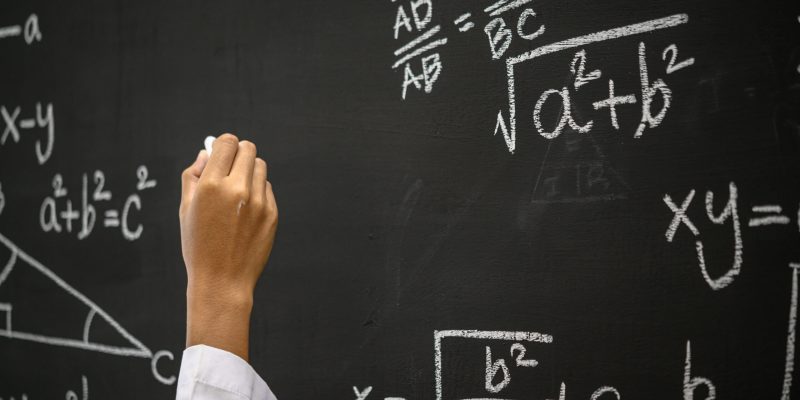 The hand that writes the formula with white chalk on the blackboard